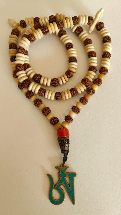 Connect with ancient Eastern wisdom. This hand-knotted mala features natural, textured Rudraksha beads paired with smooth bone-like spacers. At the center hangs a powerful Tibetan 'Om' (ཨོཾ) seed syllable pendant, a sacred sound that represents the pure e