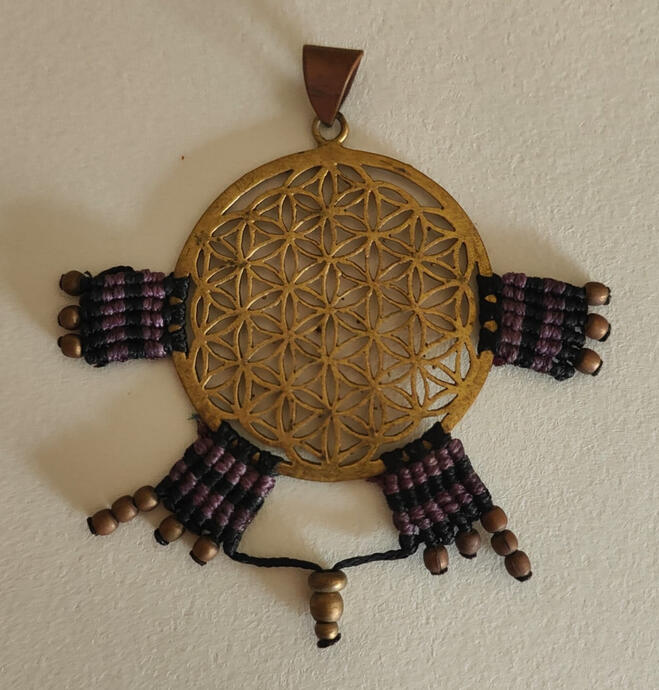 Feel the energy expand. This isn't just a pendant; it's a burst of light and intention. Featuring the sacred Flower of Life at its core, this piece radiates outward like the rays of the sun or a spiritual flame. The handwoven waxed threads in deep purple