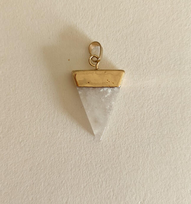Clean lines meet raw elegance. This geometric triangle pendant features a pristine white crystal with natural facets, set in a hand-finished antique brass bezel. The contrast between the sharp, modern triangle and the organic, sparkling crystal creates a