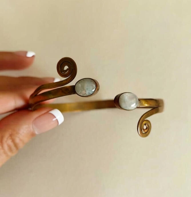 Connect with the earth through this unique Indian brass cuff bracelet. This piece features a hand-forged antique brass band with elegant swirls and an open-ended design that fits most wrists. At its heart are two raw, unpolished crystals held in place by